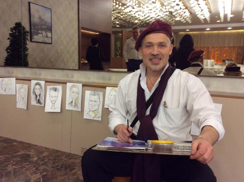 Художник сидит на фоне своих рисунков шаржист Михаил Шабалин Мишель Минск